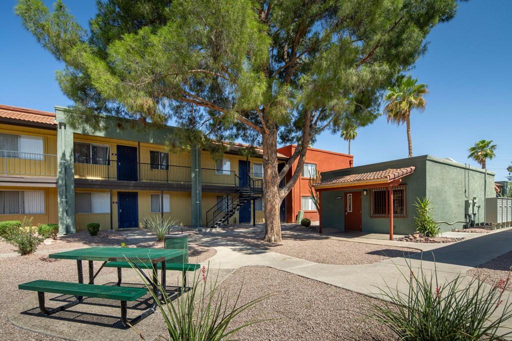 A green picnic table is in front of a building with a tree in front of it.