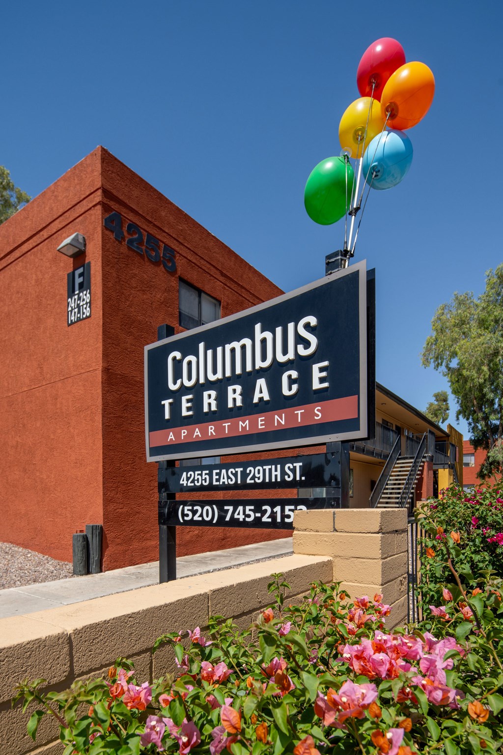 A sign for Columbus Terrace Apartments with a building in the background and balloons on top.