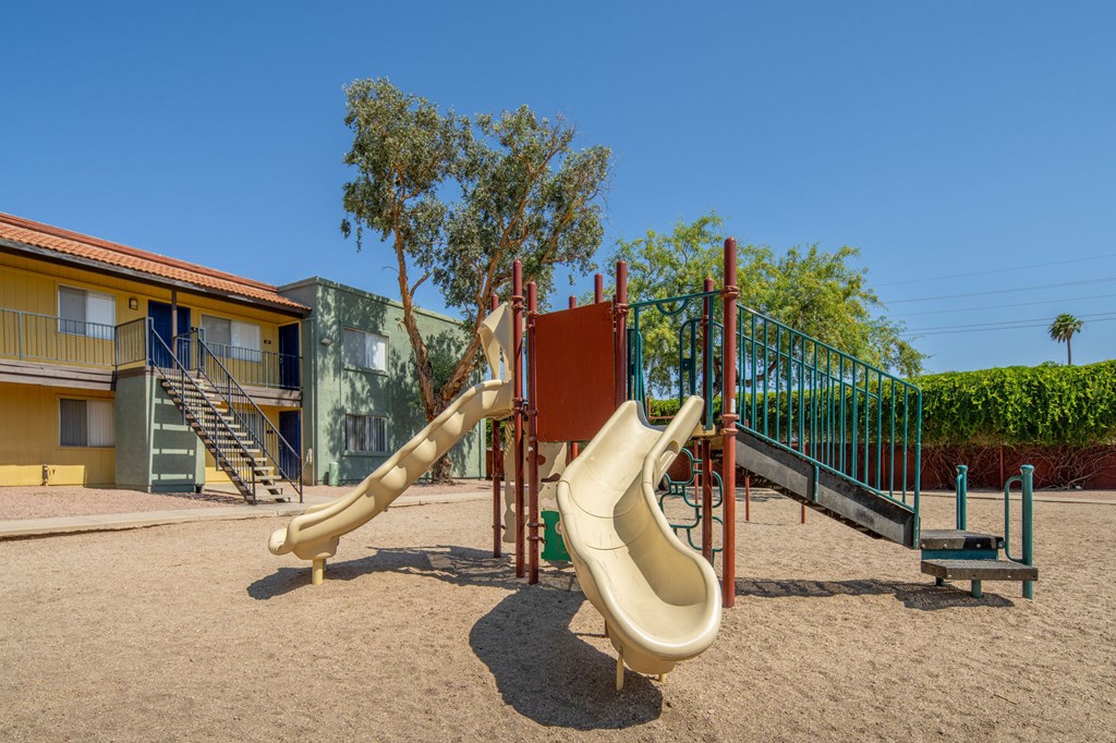 A playground with a yellow slide and a green fence.