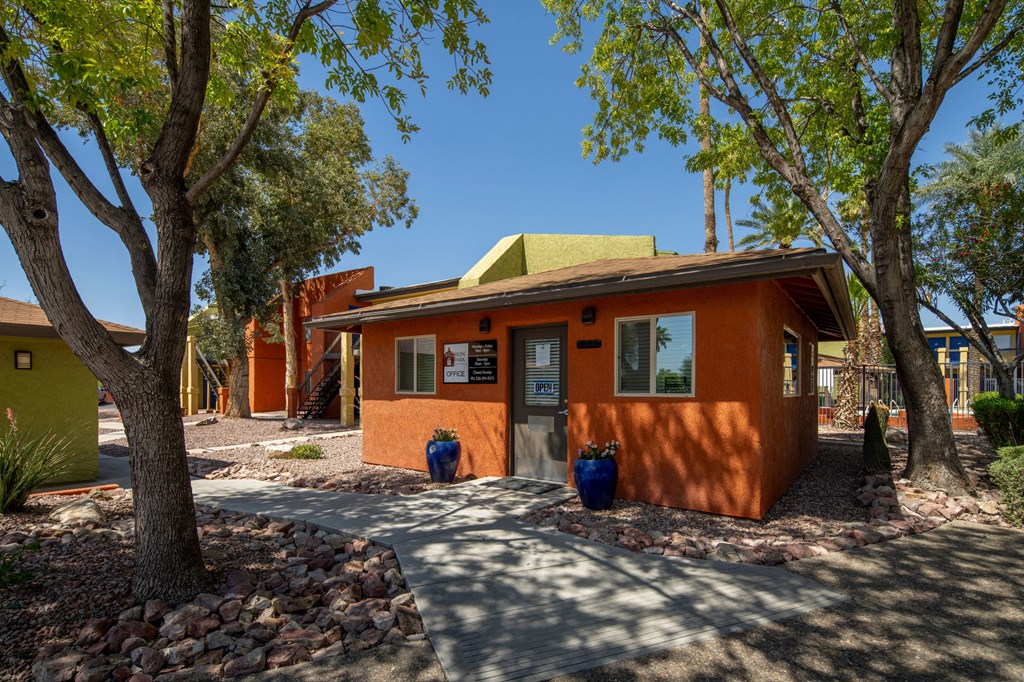 A small orange building with a green roof is surrounded by trees and has a gravel driveway in front.