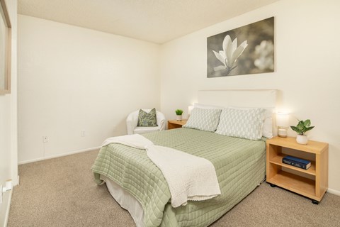 A bedroom with a bed, nightstand, and a picture on the wall.