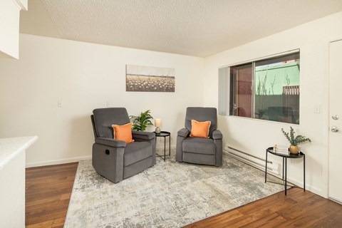 Two grey chairs with orange pillows are in a room with a grey rug.