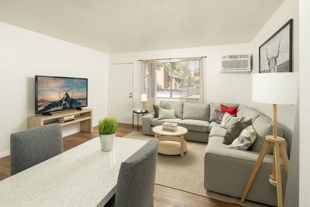A living room with a grey couch, a white dining table and a painting on the wall.