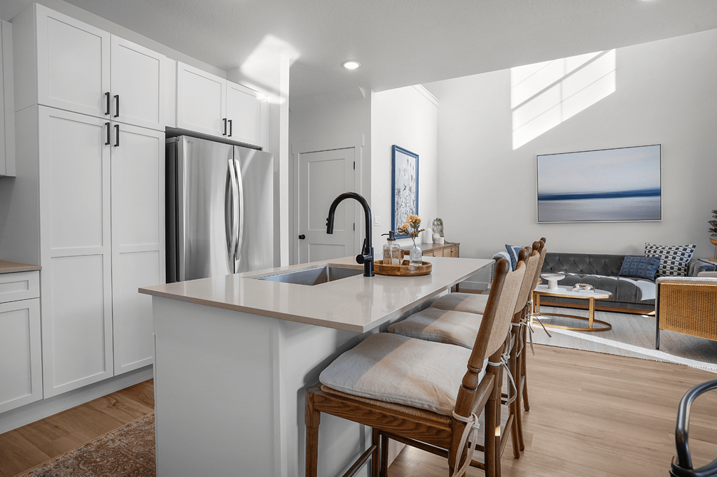 A kitchen with a refrigerator, sink, and a dining table with chairs.