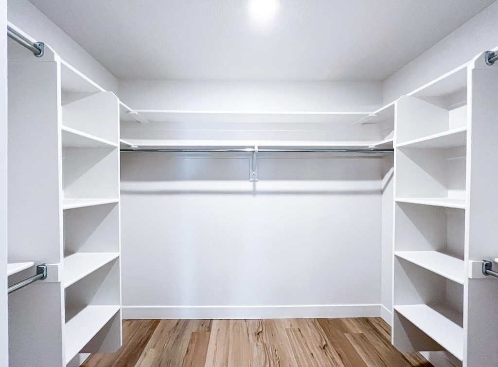 a walk in closet with white shelves and a wood floor