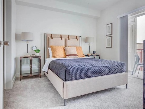 A bedroom with a large bed and a small table with a lamp.