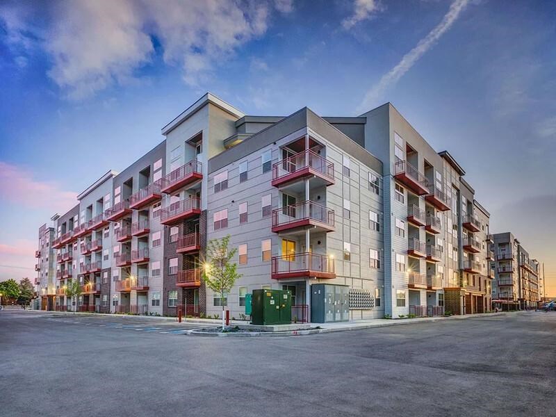A modern apartment building with balconies and a parking lot in front.