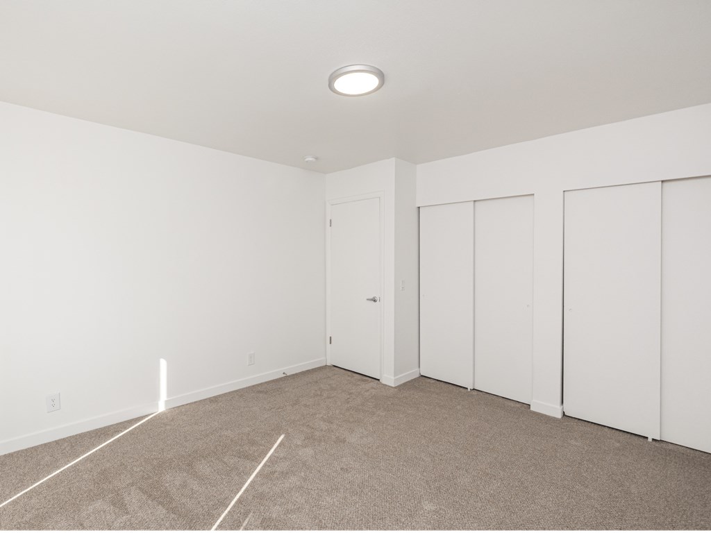 a bedroom with white walls and carpet and white closet doors