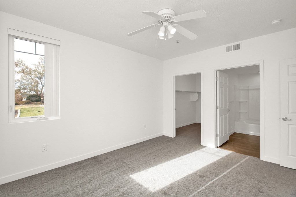an empty bedroom with a ceiling fan and a door to a bathroom