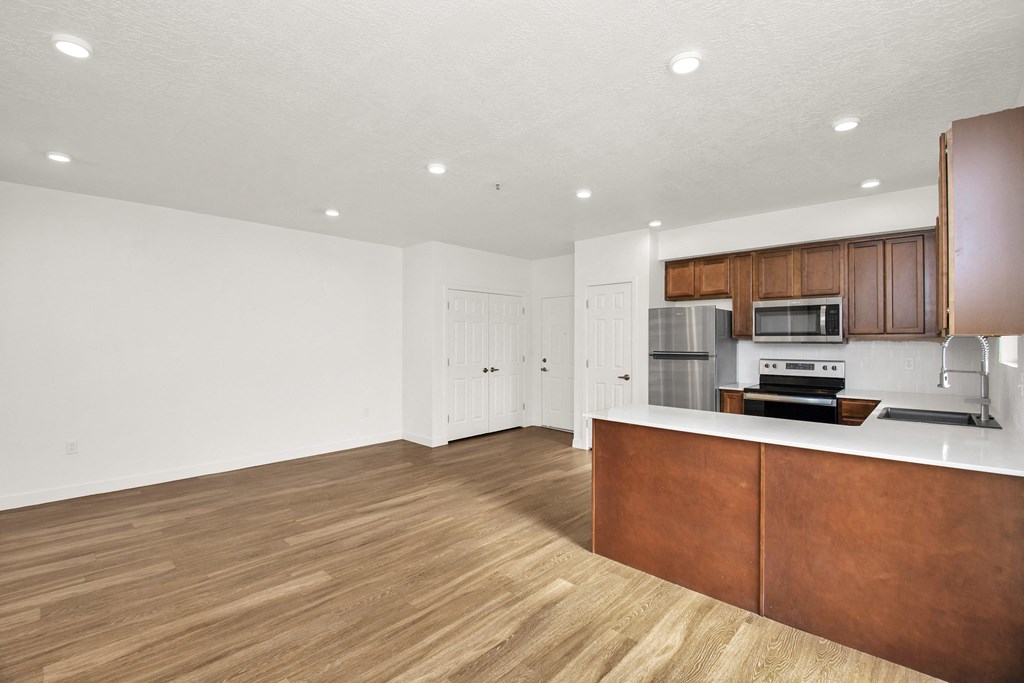 an empty living room and kitchen with wood flooring and white walls