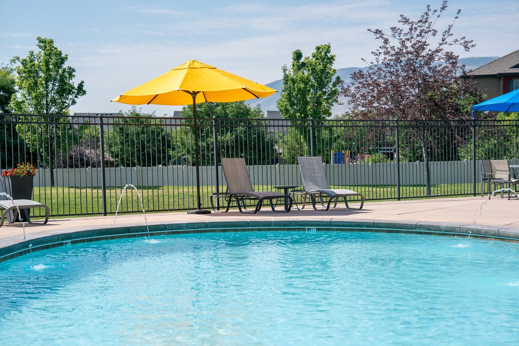 our resort style swimming pool is next to our patio with chairs and an umbrella at Aldara Apartments in Saratoga Springs, Utah