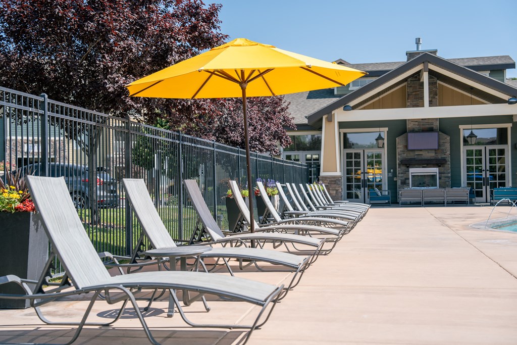 a row of lounge chairs under an umbrella in front of a building at Aldara Apartments in Saratoga Springs, Utah