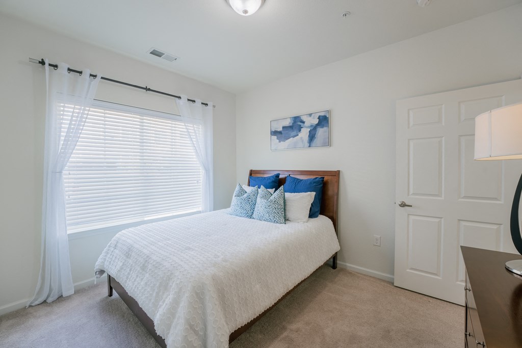 a bedroom with white walls and a bed with blue and white pillows at Aldara Apartments in Saratoga Springs, Utah
