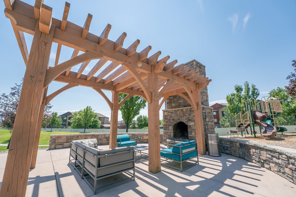 a wooden pergola with a stone fireplace and a patio with furniture at Aldara Apartments in Saratoga Springs, Utah