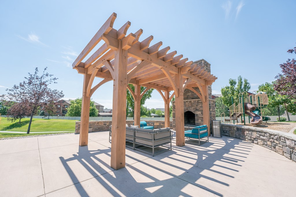 a wooden pergola over a patio with a stone fireplace at Aldara Apartments in Saratoga Springs, Utah