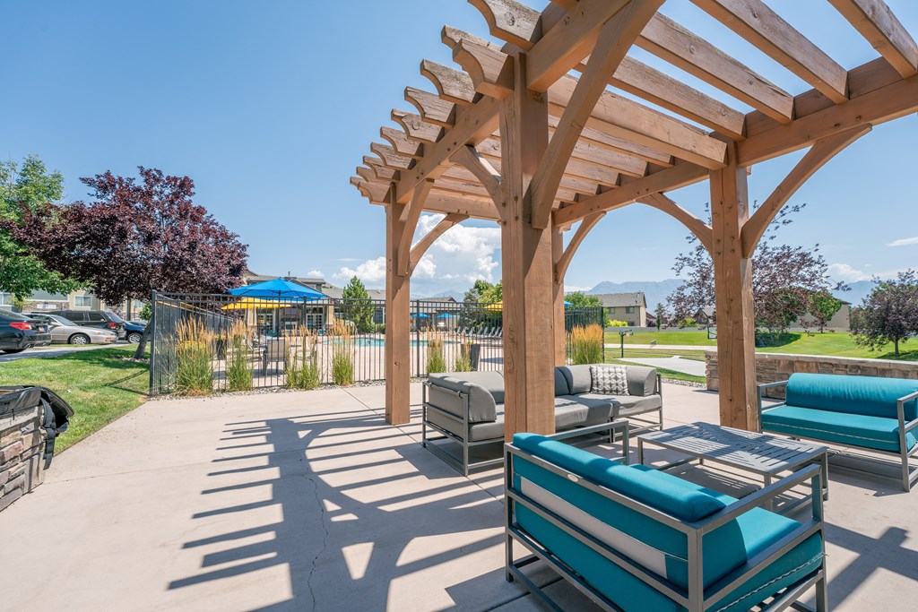 a patio with couches and a picnic table under a wooden pavilion at Aldara Apartments in Saratoga Springs, Utah