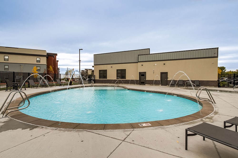 a pool with water fountains and a building in the background