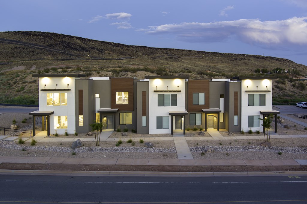 A modern building with a flat roof and large windows is illuminated from within, set against a dusky sky.