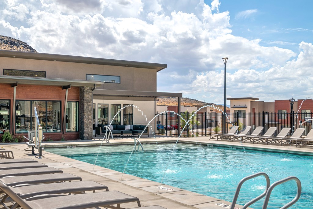 A pool with a fountain and lounge chairs in front of a building.