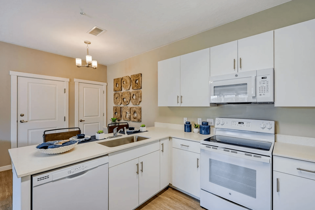 a bright and modern kitchen with white cabinets and appliances and a sink at Brookfield Apartments for rent in St. George, UT.