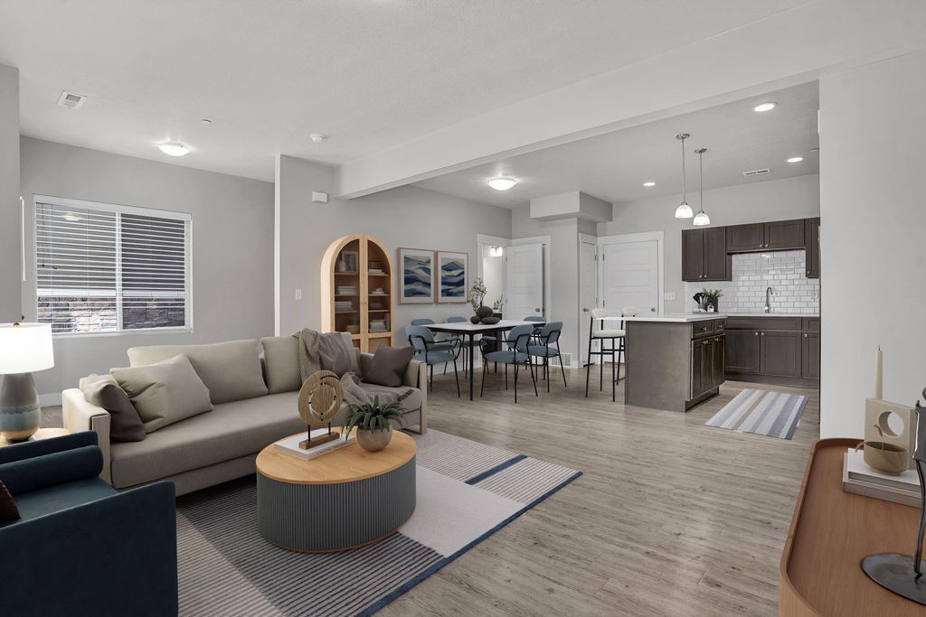 A modern living room with a grey sofa, a wooden coffee table, and a dining area in the background.