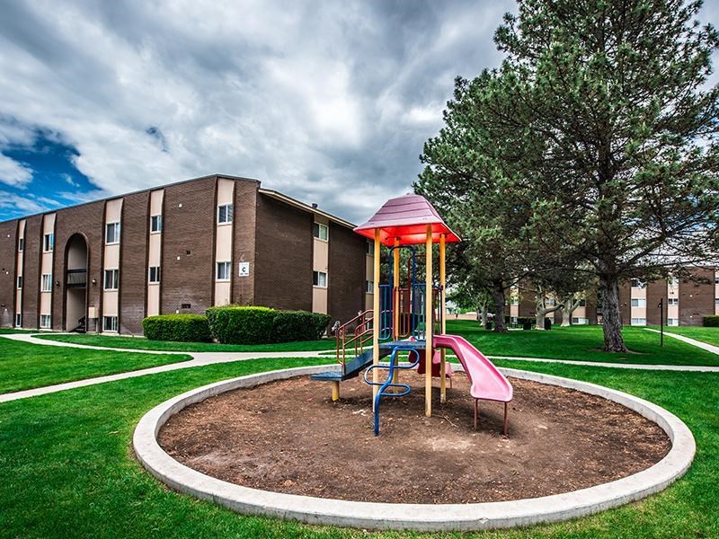 A playground with a red roof and a slide is in the foreground of a building.