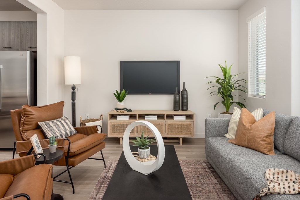 A living room with a grey sofa, a brown chair, a black coffee table, a flat screen TV, and a wooden cabinet.