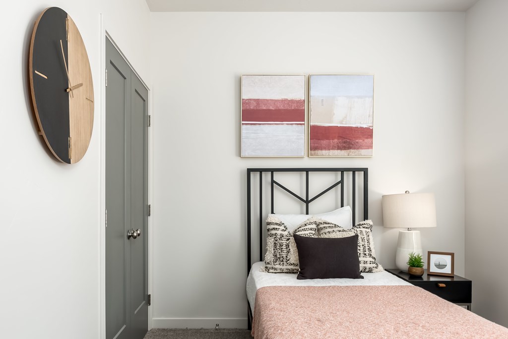A bedroom with a bed, nightstand, lamp, and a clock on the wall.