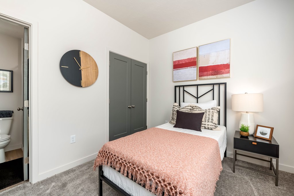 A bedroom with a bed, nightstand, and a clock on the wall.
