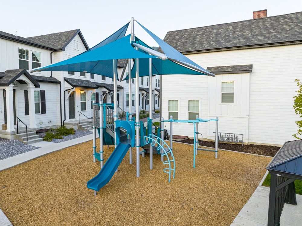 a playground with a blue slide and umbrella in front of a white building