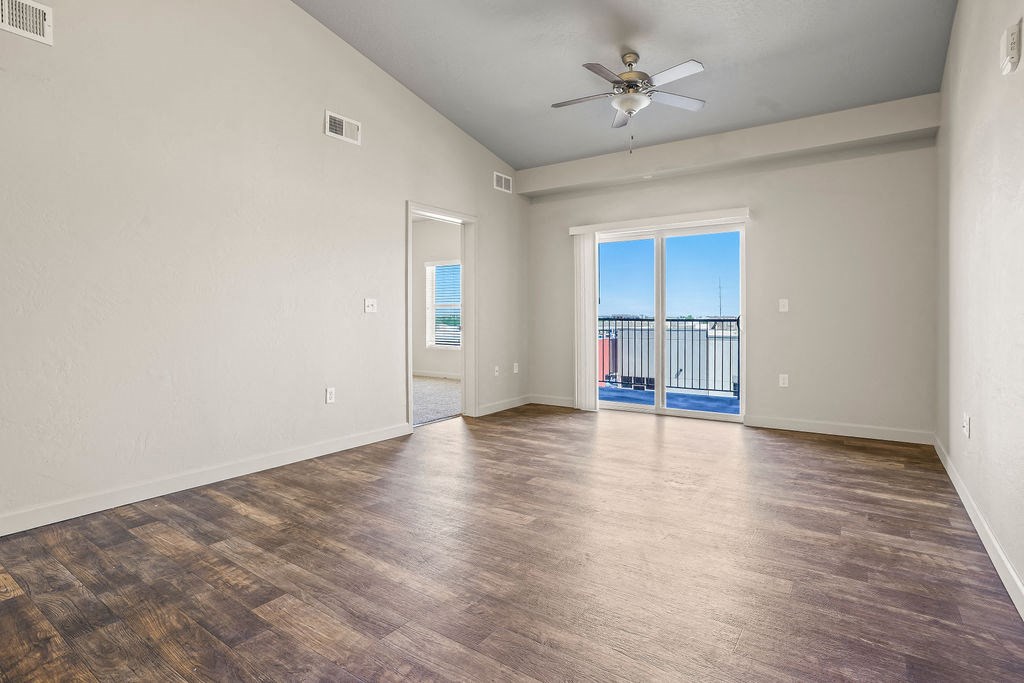 an empty living room with a ceiling fan and a balcony