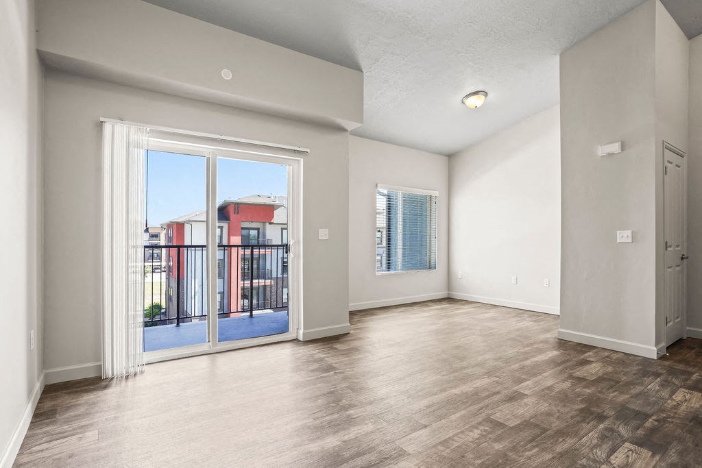 an empty living room with a sliding glass door to a balcony