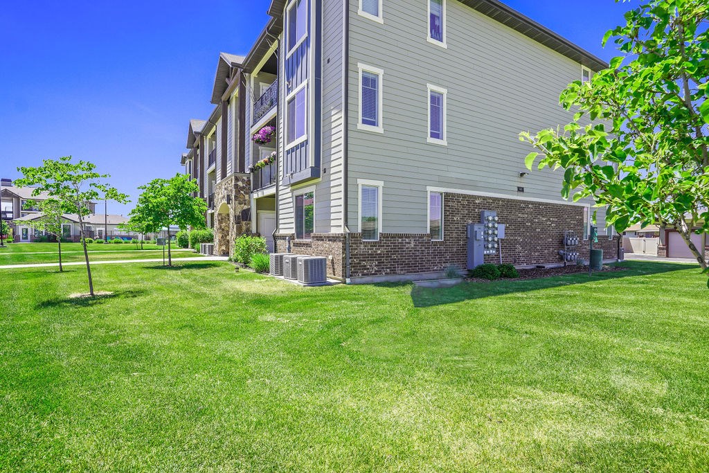 A grassy area in front of a building with a brick wall and a tree.