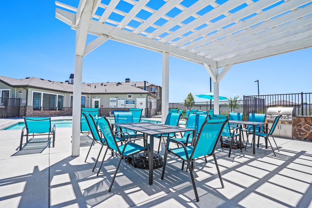 A white pergola with blue chairs and a table is set up on a patio.