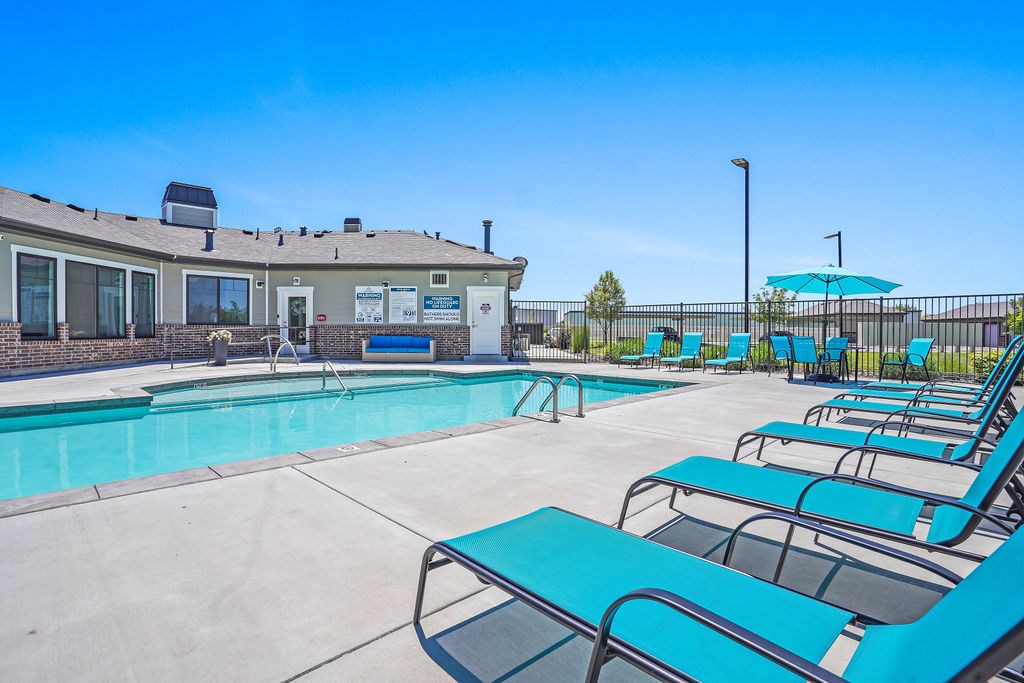 A sunny day at the pool with blue lounge chairs and a building in the background.