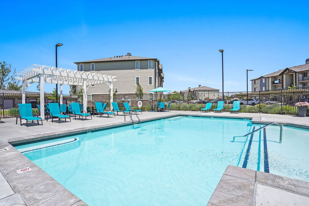 A swimming pool with a white pergola and blue lounge chairs.