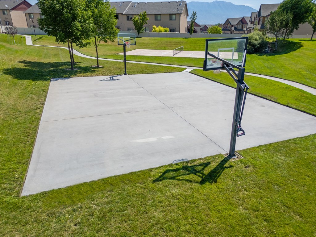 a basketball hoop on the grass next to a concrete court at Aldara Apartments in Saratoga Springs, Utah