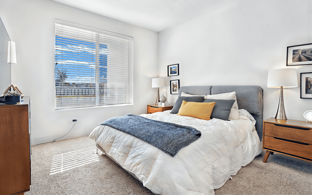 A bedroom with a large bed and a window with blinds.