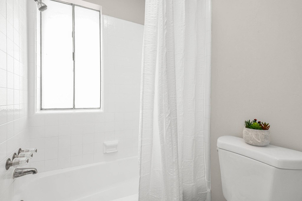 A white bathroom with a tub, toilet, and a window.
