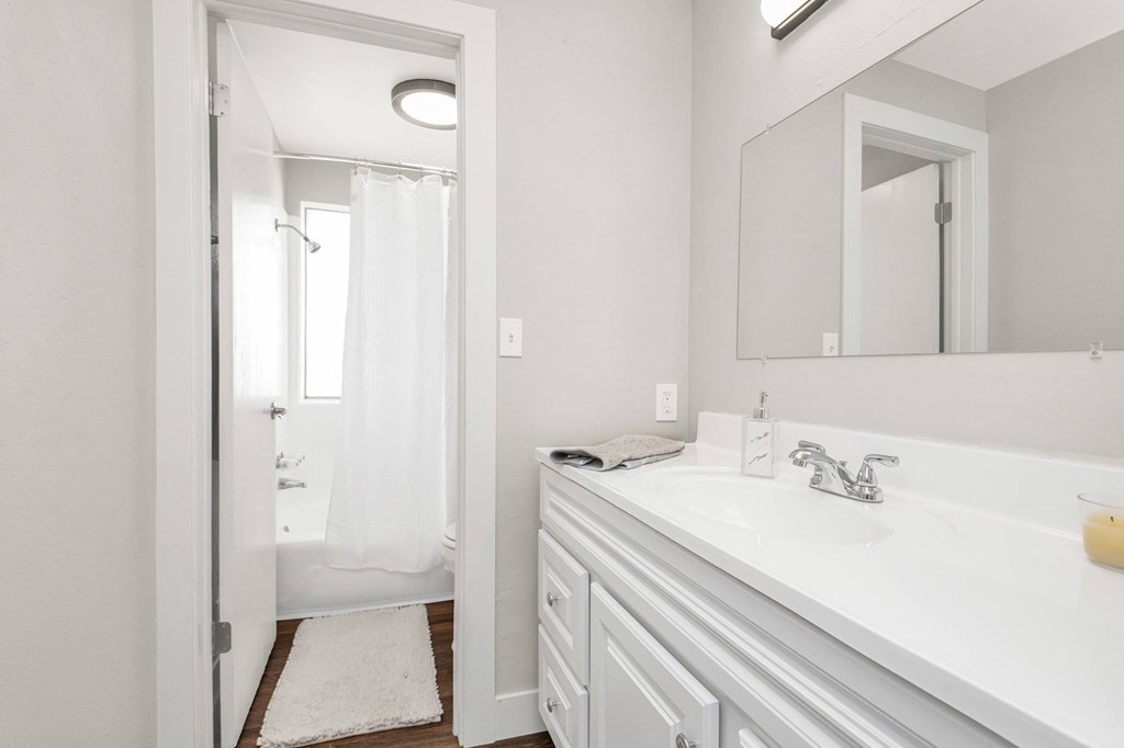 A white bathroom with a sink, mirror, and shower.