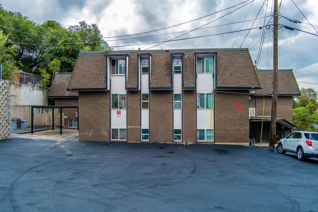 A parking lot in front of a brick building with a car parked.