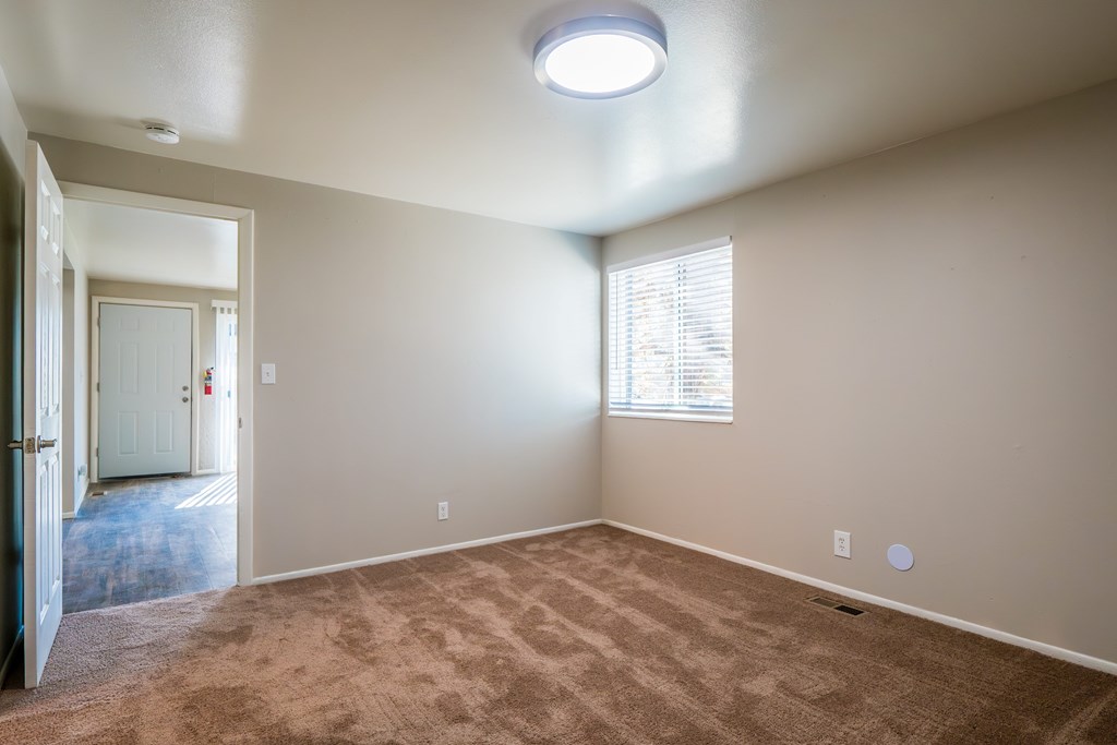 A room with a carpeted floor and a window with blinds.