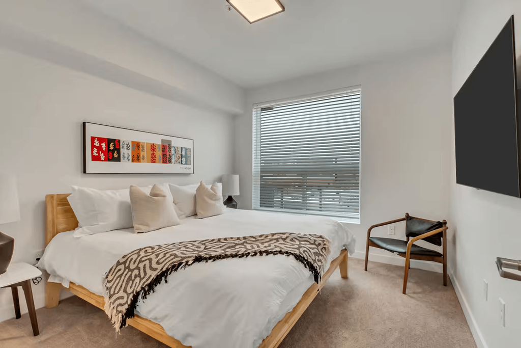 A bedroom with a bed, chair, and a painting on the wall.