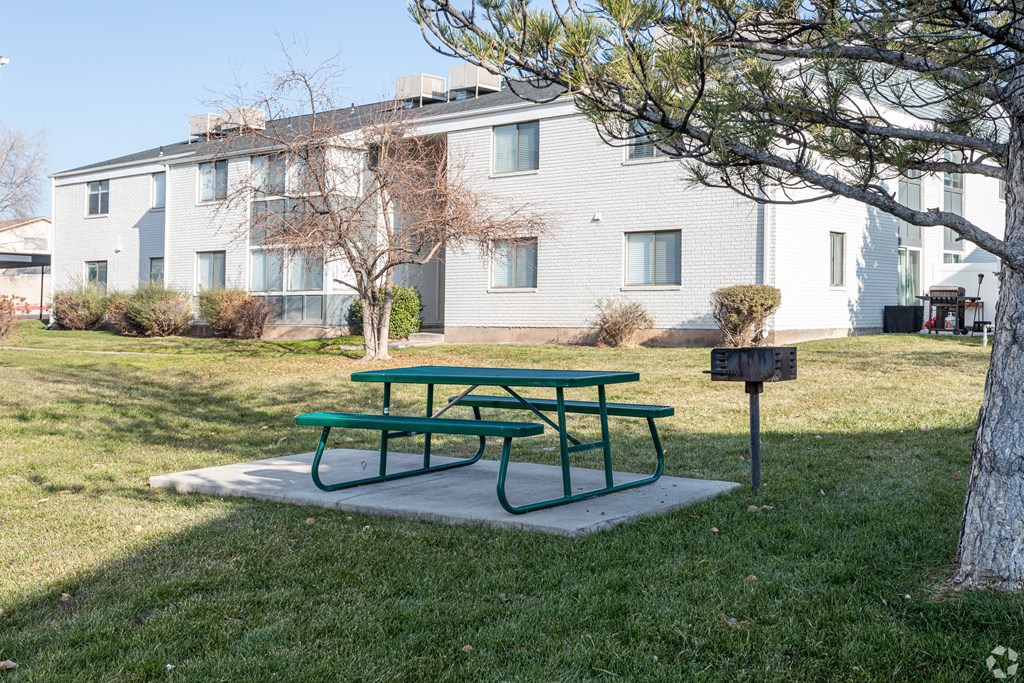 A green picnic table sits in front of a grey building.