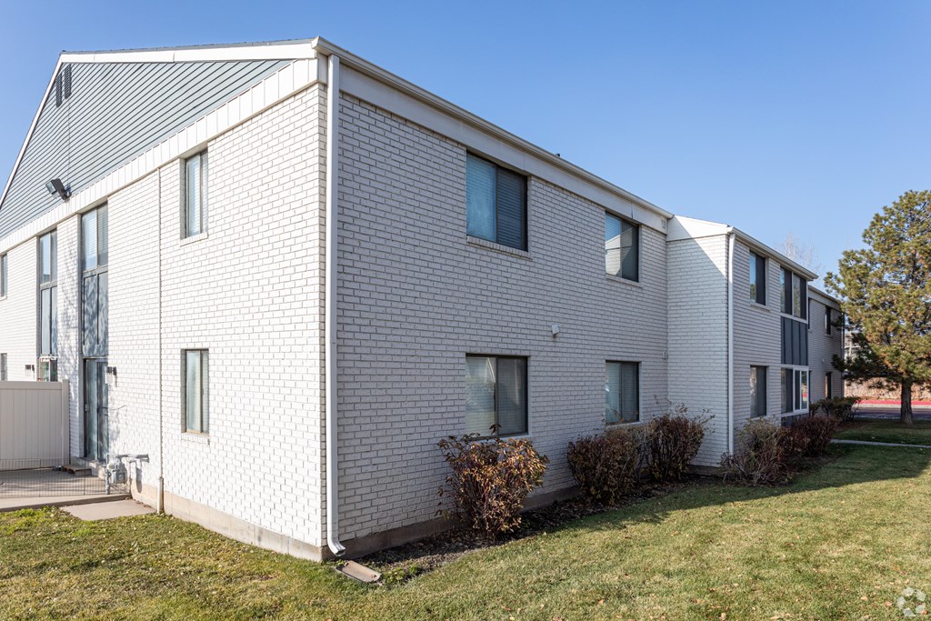 A white brick house with a grey roof and a green lawn in front.