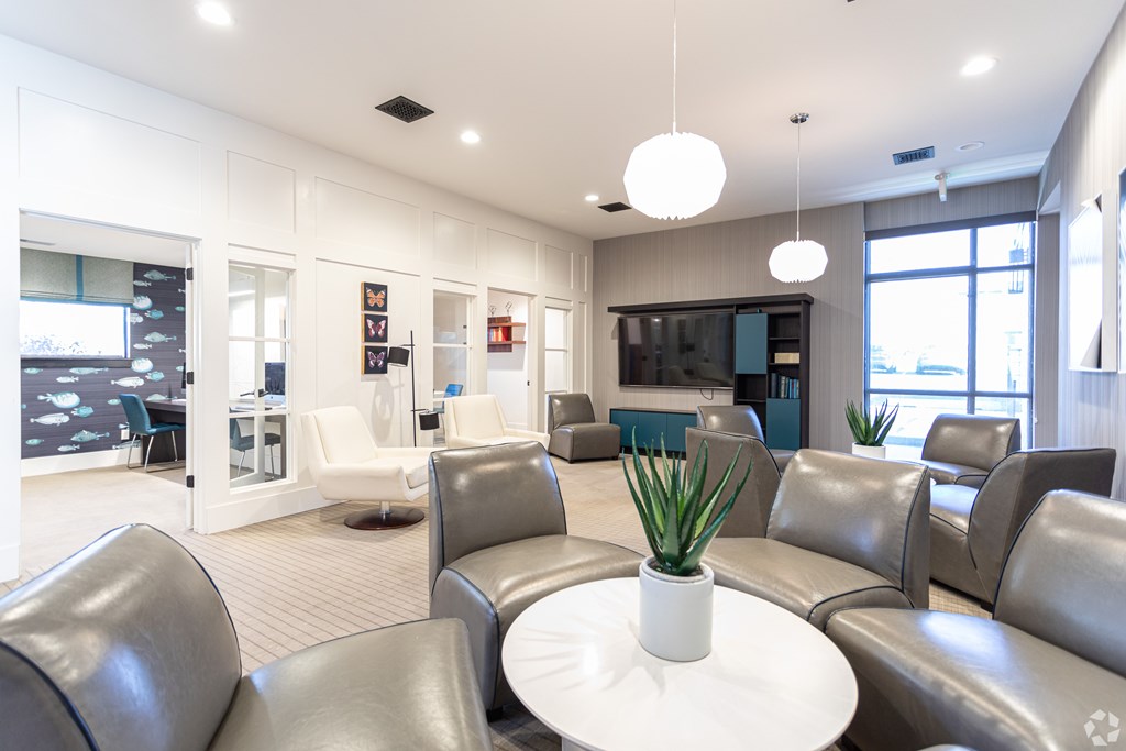 A white table with a plant on it sits in the middle of a room with grey couches.