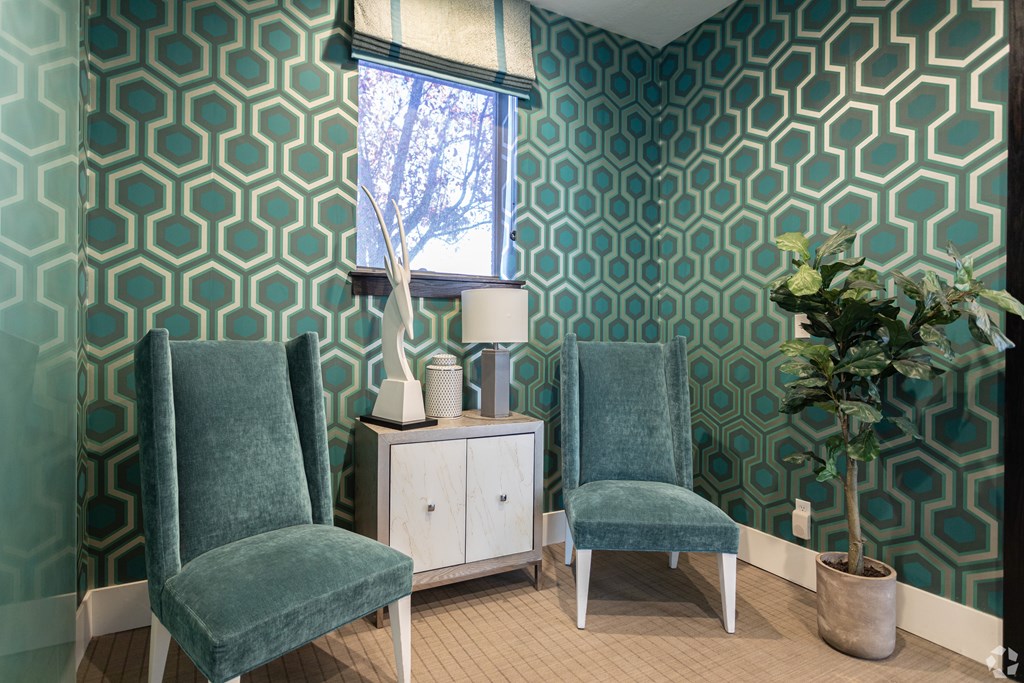 Two green chairs sit in front of a patterned wallpapered wall.