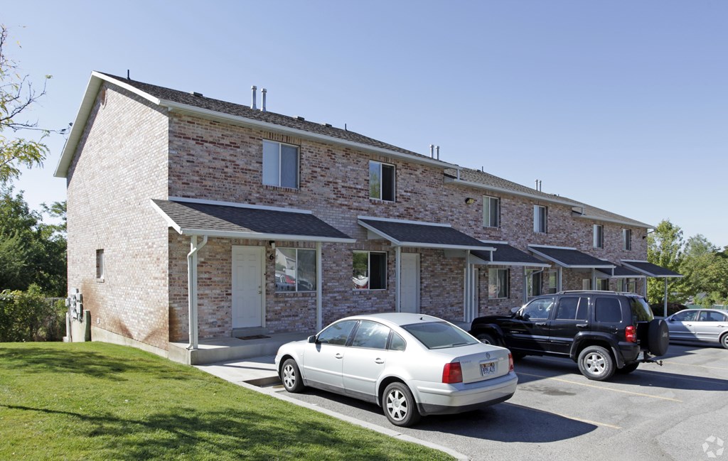 A silver car is parked in front of a house with a black car behind it.