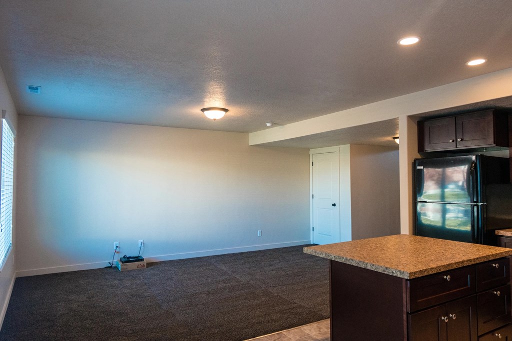 an empty living room with a kitchen and a refrigerator