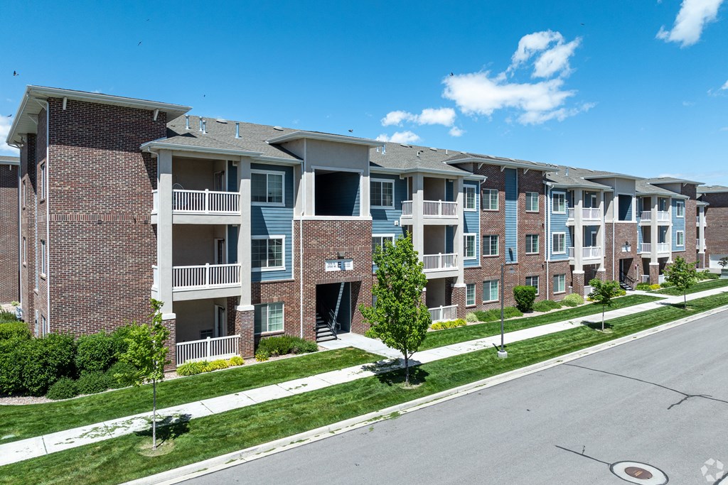 an apartment building on a city street with grass and trees at Outlook Apartments for rent in Springville and Provo, UT.